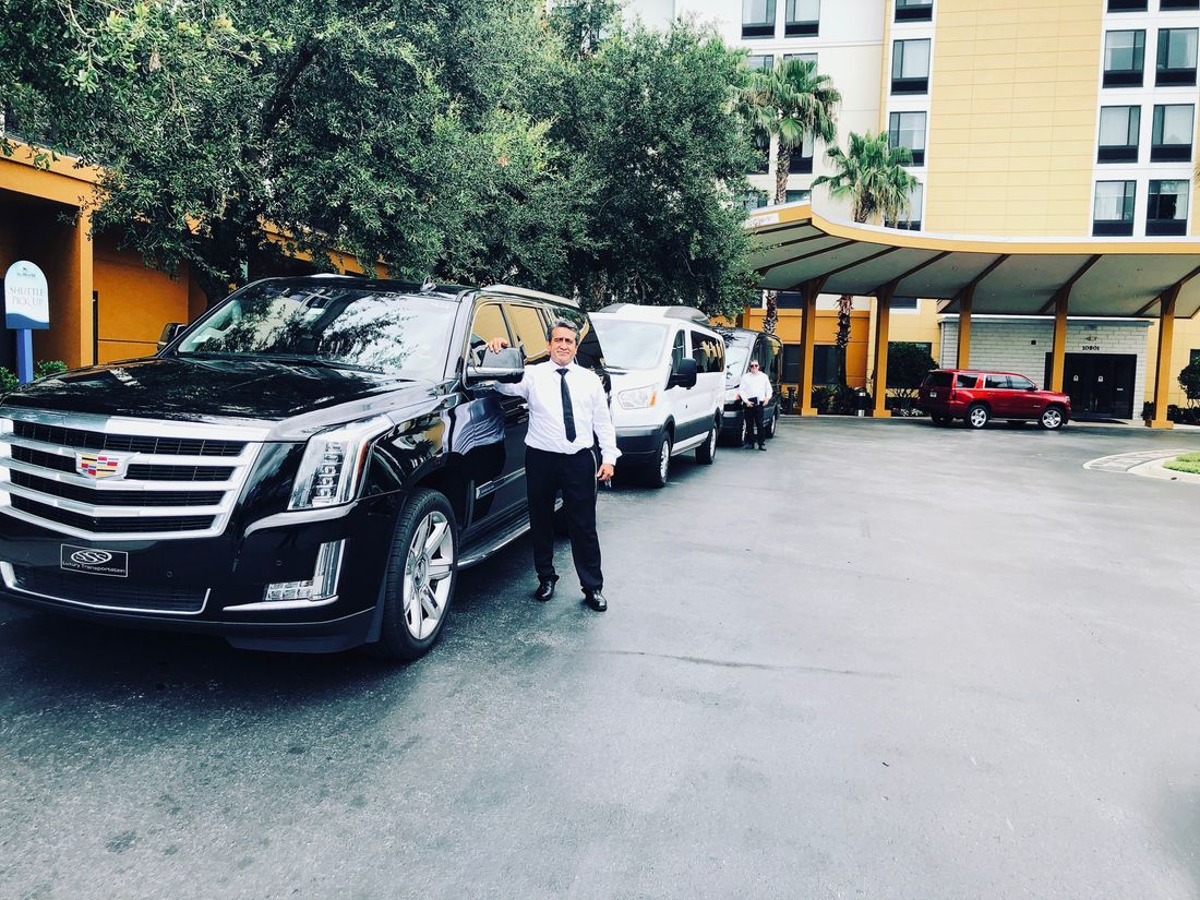 Chauffeurs beside black Escalades at a resort entrance